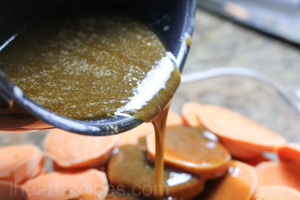 Pouring candied syrup over sliced sweet potatoes in a glass dish.