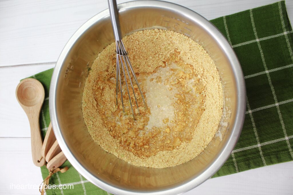 An overhead image of a metal bowl and a whisk mixing up a graham cracker crust for the key lime Jello cheesecake recipe.