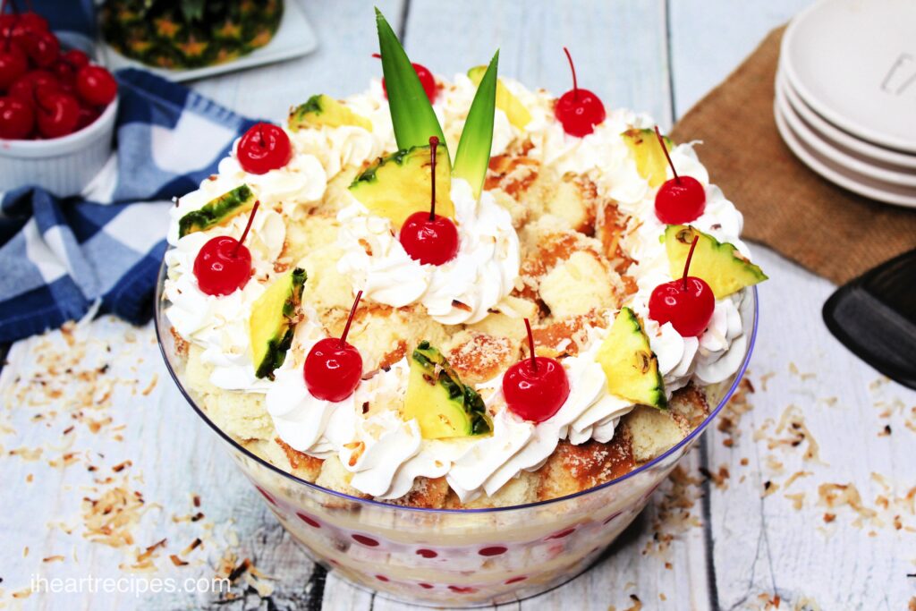 An overhead angled image of a pina colada cake trifle with layers of poundcake, pineapple and cherry whipped cream filling, and a pineapple and cherry garnish on top.