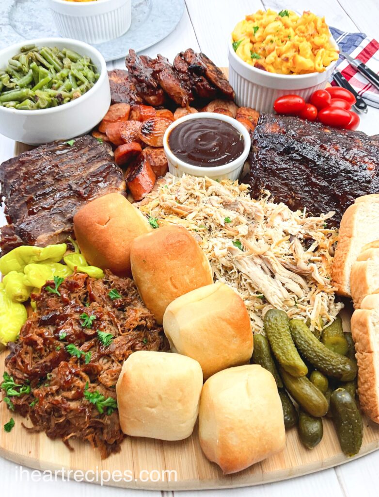 A leftovers charcuterie board packed with leftover BBQ meats like pulled pork, chicken and ribs, dinner rolls, sauces, pickles and sides like green beans and mac and cheese.