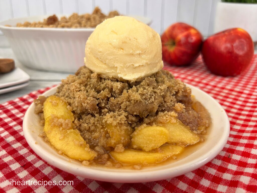 A small bowl filled with fresh homemade apple crisp - sliced apples baked and topped with a streusel crumble topping, and a scoop of vanilla ice cream.