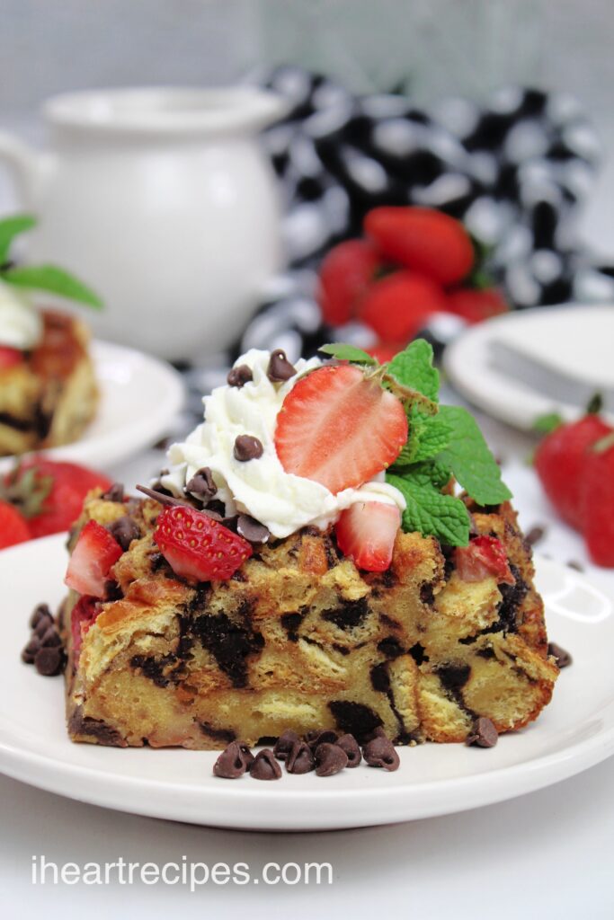 A serving of tender and moist French bread casserole topped with sweet whipped cream, sliced strawberries and chocolate chips. 
