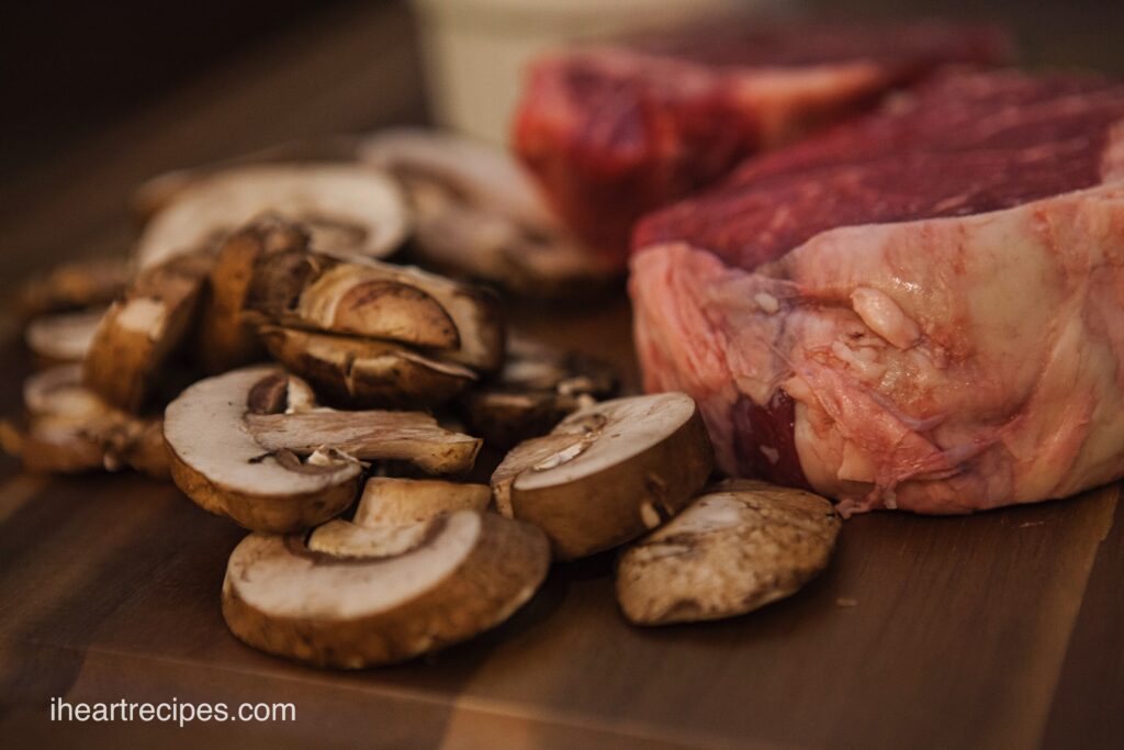 Some ingredients for filet mignon with herb butter mushrooms sit on a wooden cutting board. 