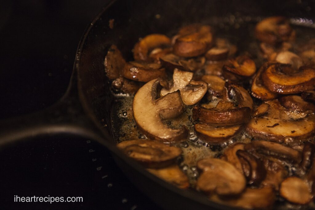 Golden sliced mushrooms sautéing in a cast iron skillet.  