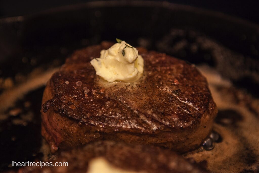 A tender filet mignon with a dollop of herb butter sizzling on a cast iron skillet. 