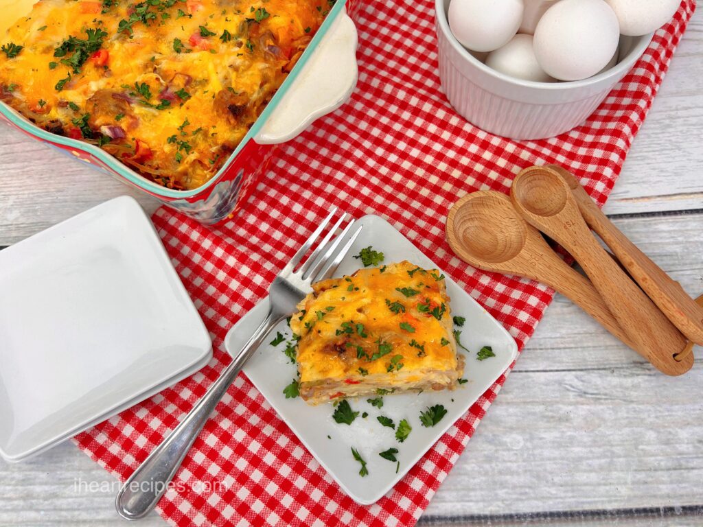 An overhead image of hash brown casserole -- a slice served on a plate, and a whole casserole dish.  Around the casserole is a dish of eggs, wooden serving spoons and serving plates.