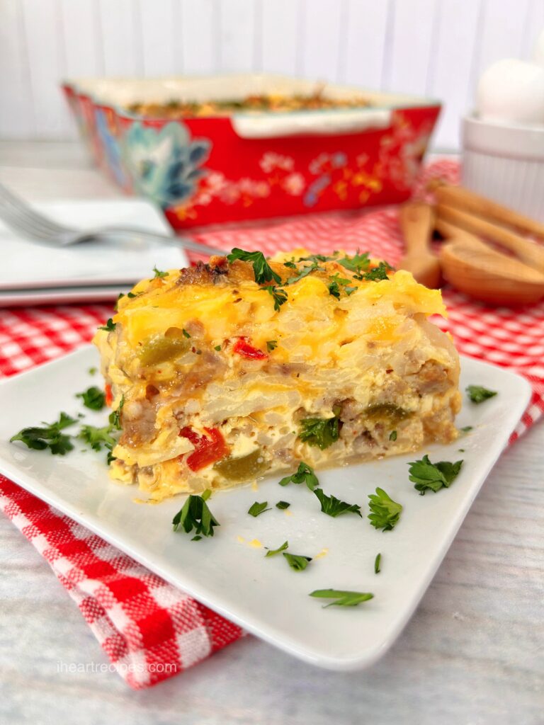 A close up image of a slice of hash brown casserole, made with layers of frozen hash browns, sausage, veggies, and cheese.