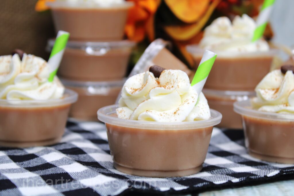 Stacks of pumpkin latte Jello shots made in small condiment cups, topped with whipped cream.