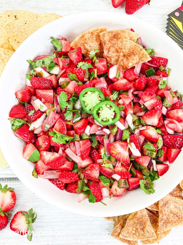 Strawberry and jalapeño pico filled with bright red strawberries, fresh jalapeños, crispy red onions and fresh cilantro. It's served in a large white bowl and garnished with cinnamon tortilla chips. 