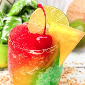 A red, yellow, and green slushy margarita served in a glass.