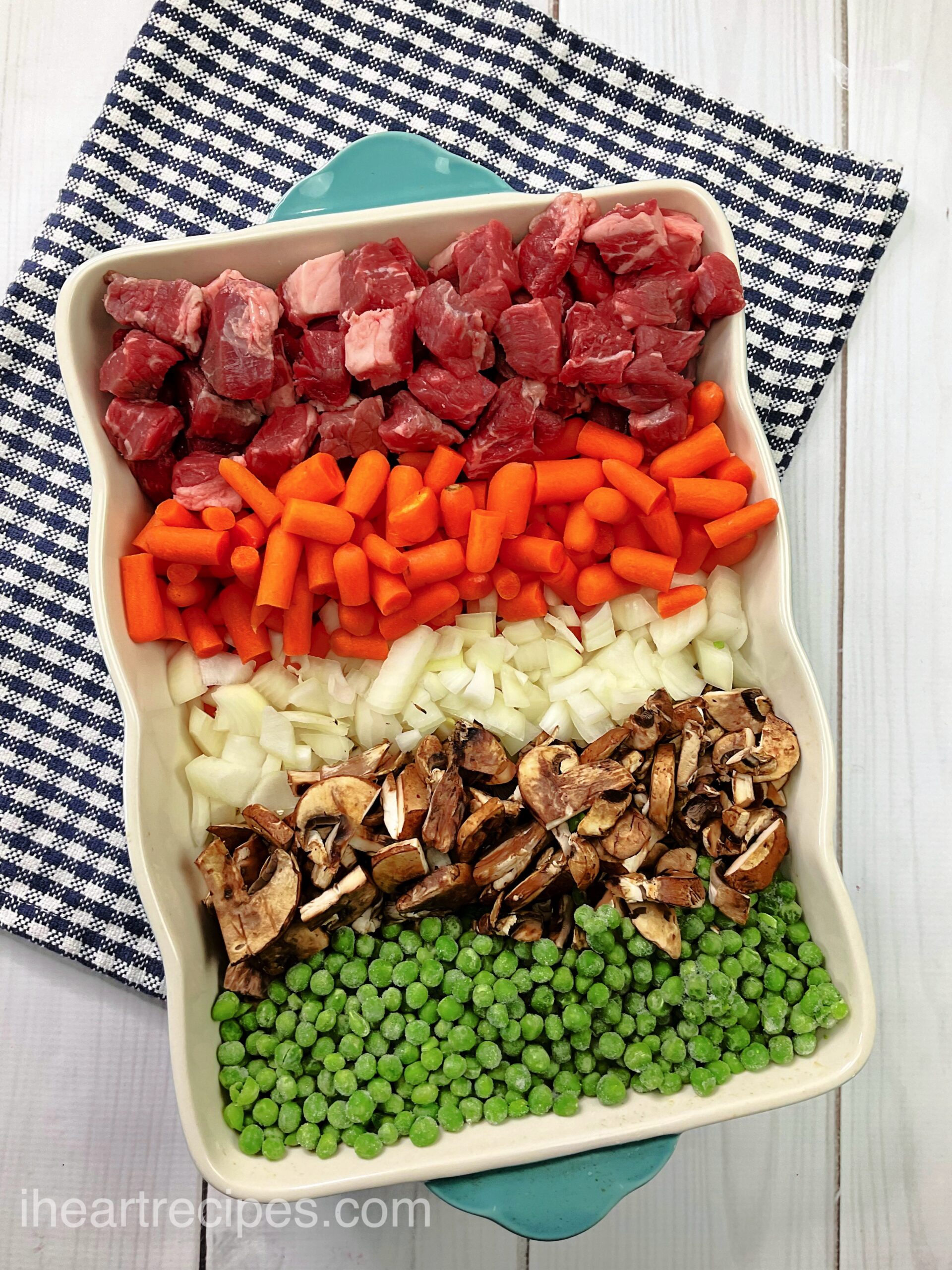 Ingredients for homemade beef pot pie laid out on a tray -- cubed beef, baby carrots, onions, mushrooms, and peas.