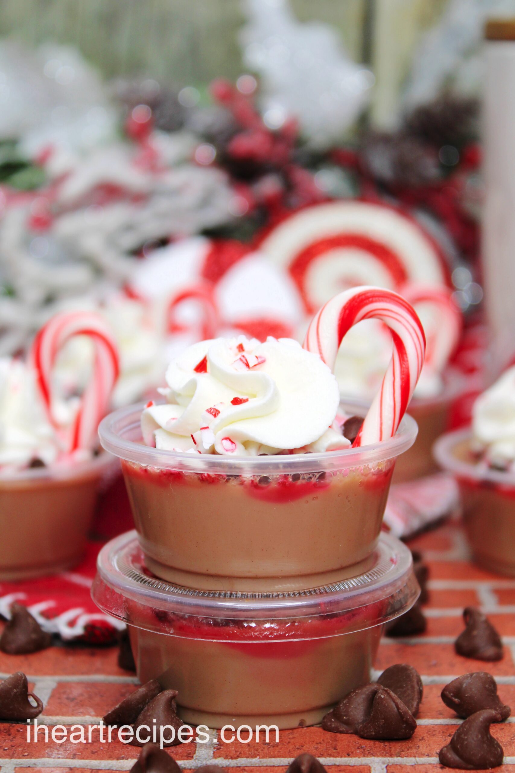 A close-up image of peppermint and chocolate Jello shots. Two are stacked on top of each other in little cups, garnished with whipped cream, mini candy canes, and chocolate chips.