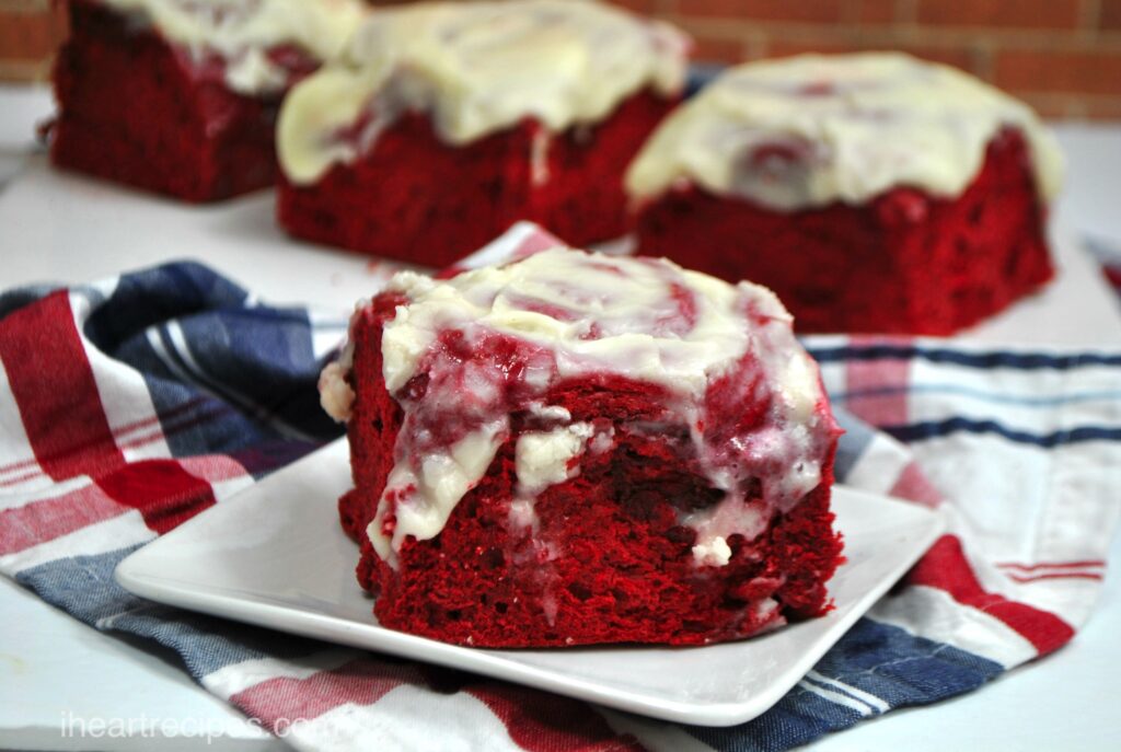 Moist red velvet cake mix cinnamon rolls topped with a sweet cream cheese frosting set on a festive red, white and blue tablecloth. 