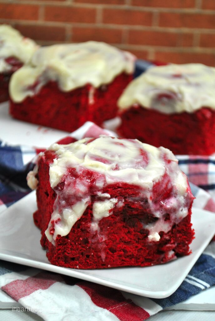 A close-up shot revealing the moist and tender red velvet roll with creamy frosting dripping down the side. 