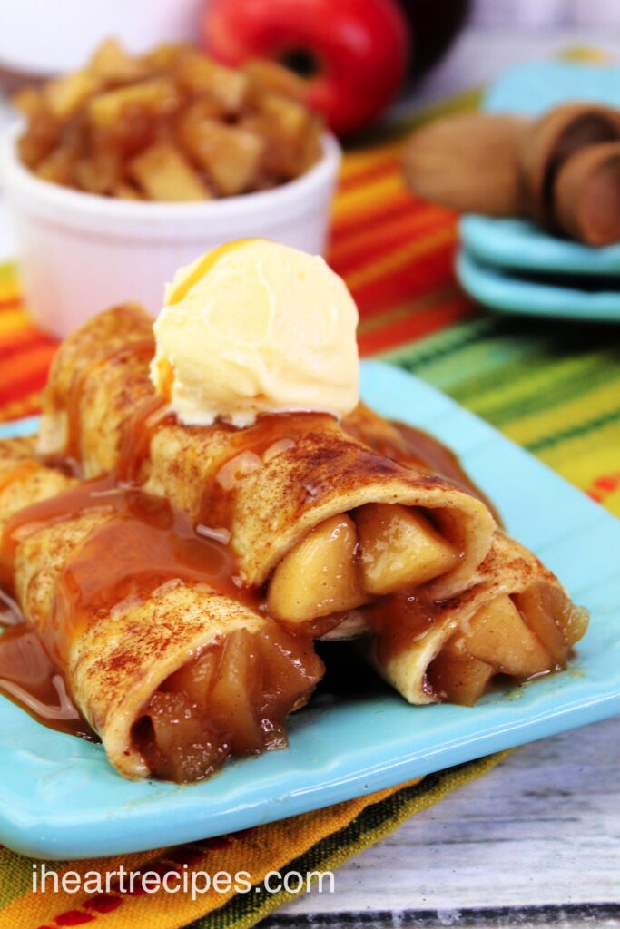 A close up image of three caramel apple taquitos, filled with apple pie filling and topped with homemade caramel sauce and ice cream.