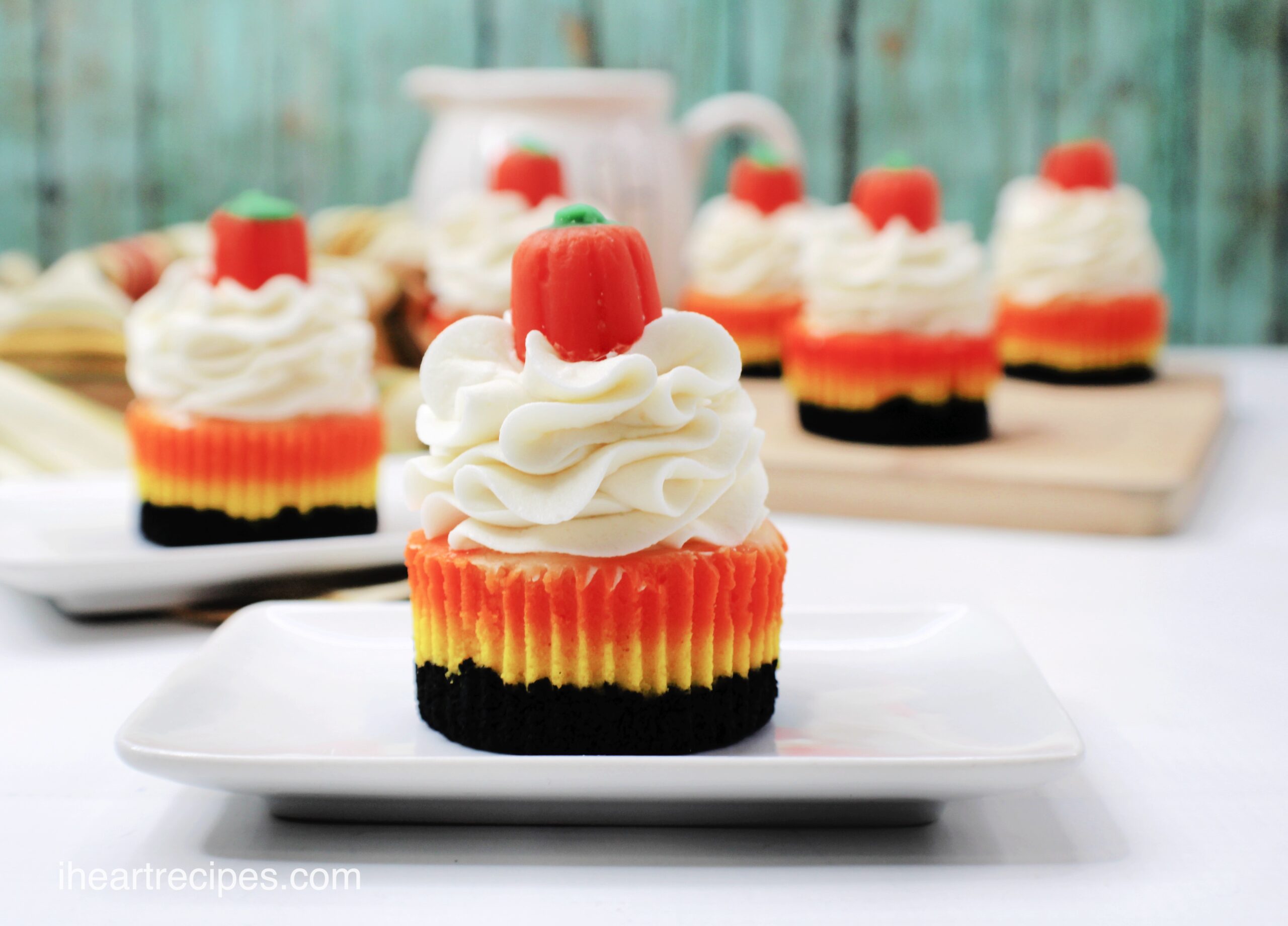 Multiple mini candy corn cheesecakes sit on small plates, each one topped with whipped cream and a candy pumpkin.