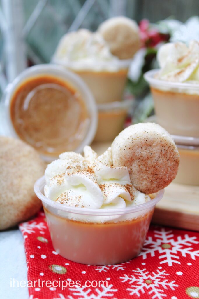 A serving of golden pudding topped with fluffy whipped cream sprinkled with cinnamon and topped with a mini cookie. 