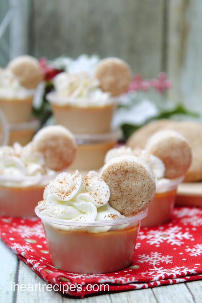 Rows of golden Snickerdoodle Jello Shots set on a red, white and gold snowflake tablecloth. 