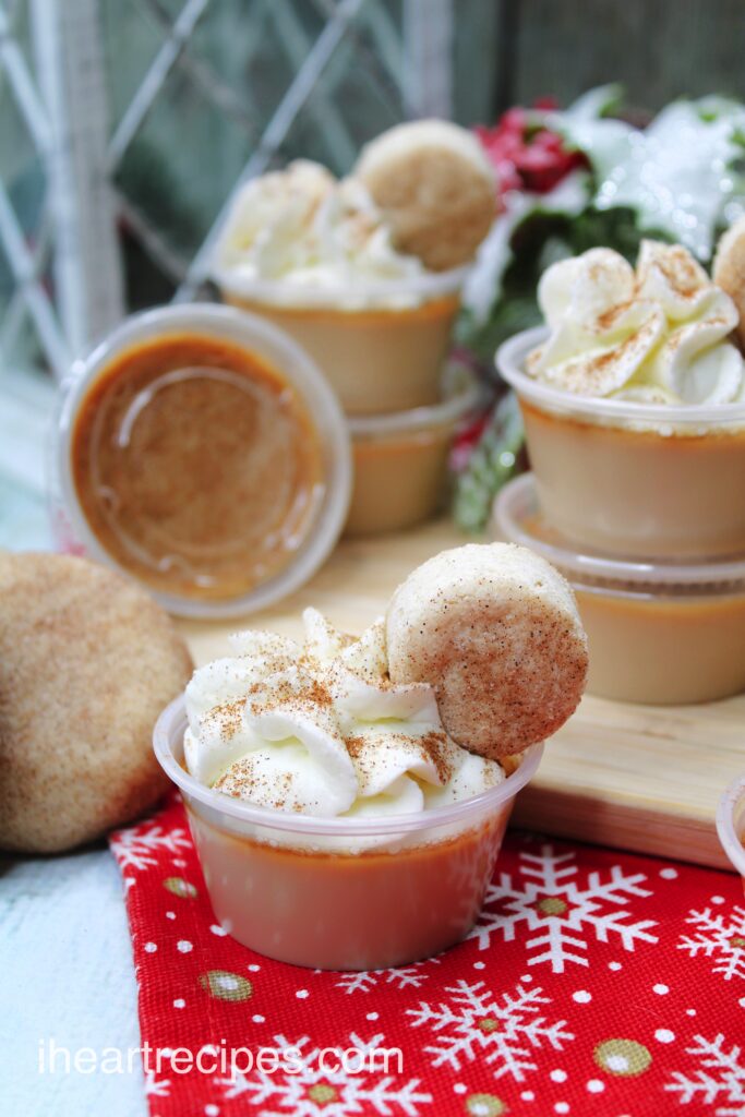 Miniature cups filled with golden Snickerdoodle Jello Shots topped with whipped cream, a tiny Snickerdoodle cookie and sprinkled with cinnamon.