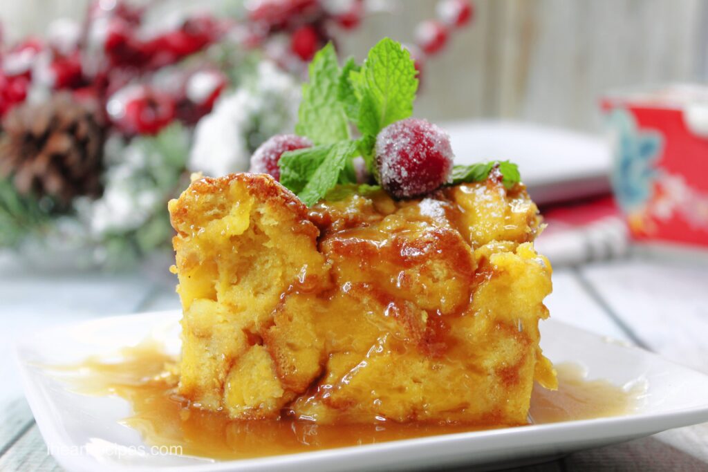 Layers of creamy eggnog bread pudding drenched in a brown sugar glaze topped with sugared cranberries and mint leaves. 