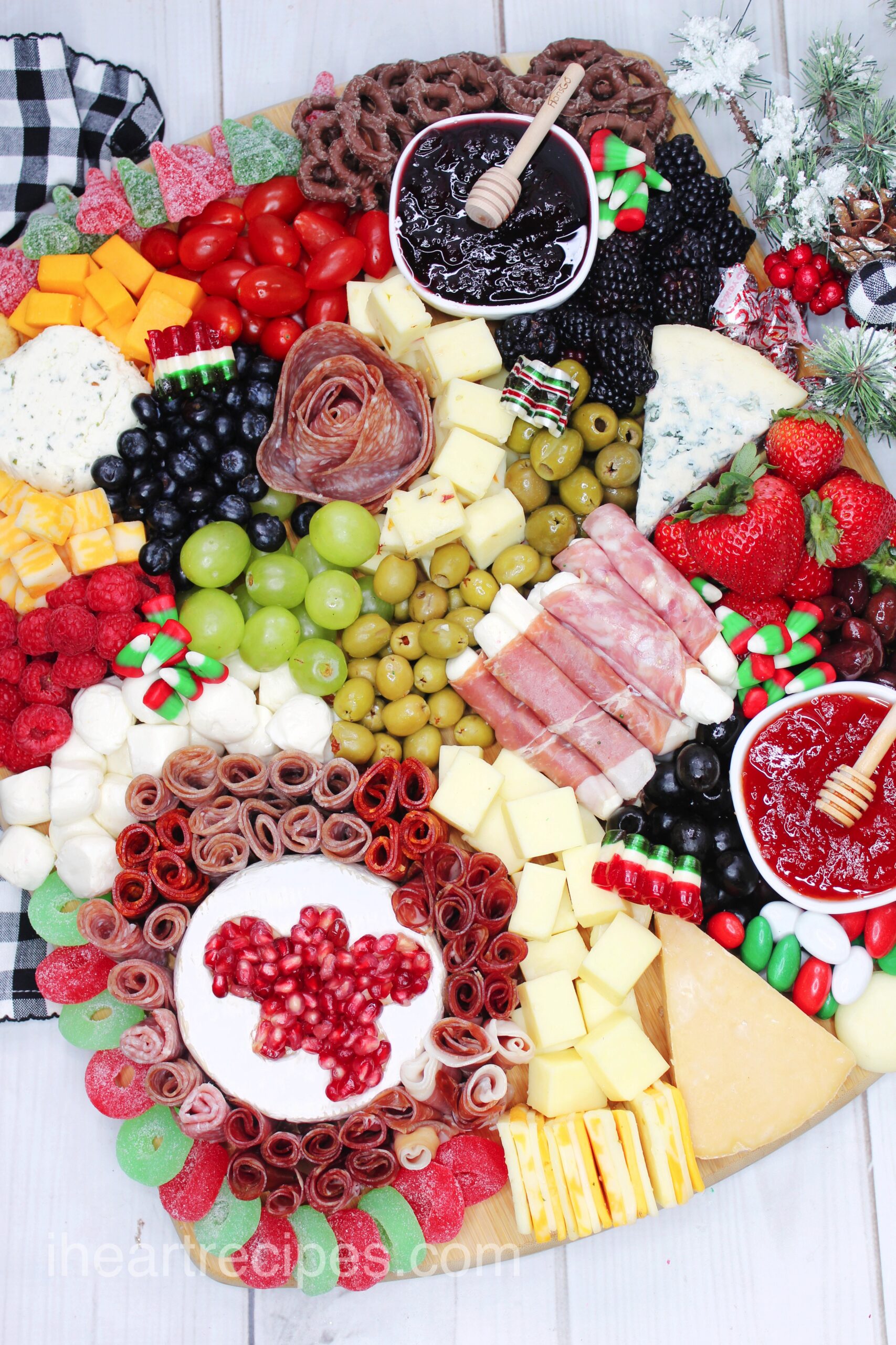 An overhead image of a full Charcuterie Board, packed with a variety of meats, cheeses, fruits, vegetables, and other Christmas treats like candies, jams, and jellies.