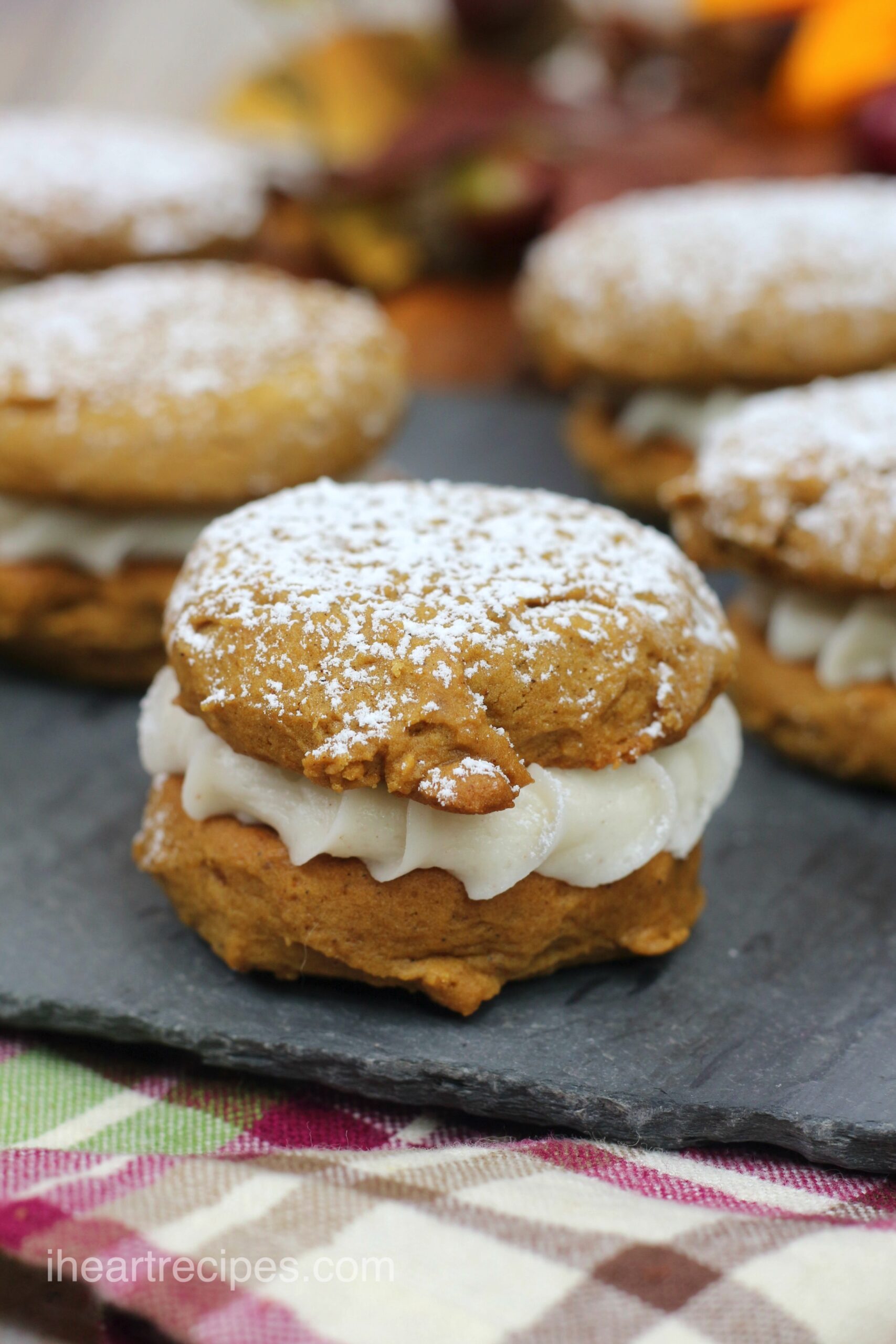 A close up image of a pumpkin gingerbread whoopie pie, filled with sweet cream icing and dusted with powdered sugar.