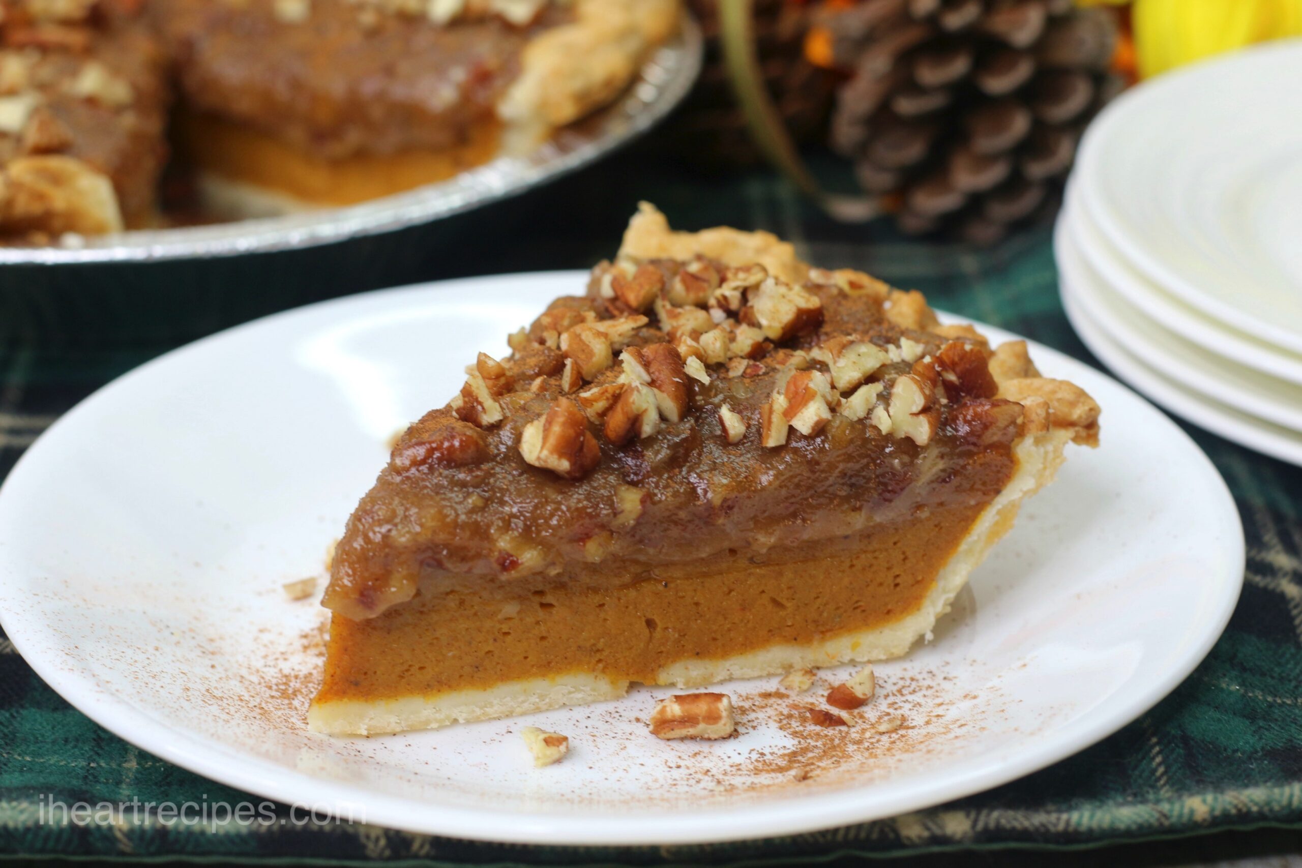 A single slice of pecan pumpkin pie served on a white plate, topped with chopped pecans and cinnamon.