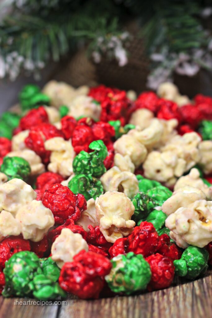 A serving of red, green and white Christmas popcorn. The bottom of a pine tree dusted with snow is in the background. 