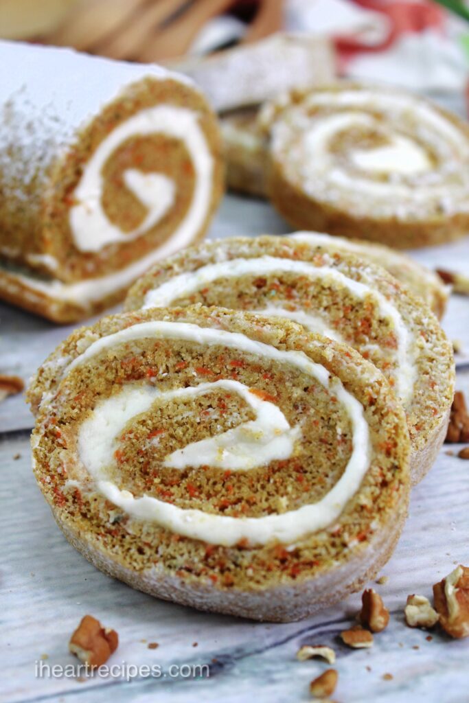 A closeup image of slices of rolled carrot cake. Ribbons of cream cheese frosting run through orange speckled cake. 