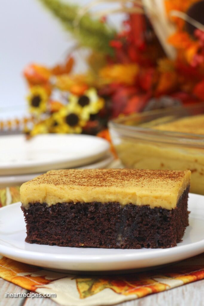 A close up of a square of moist chocolate cake topped with a creamy pumpkin frosting dusted with cinnamon.  