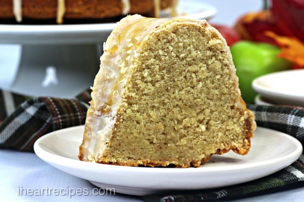 A slice of Caramel Apple Cider Cake served on a white plate. There are festive fall decorations in the background. 