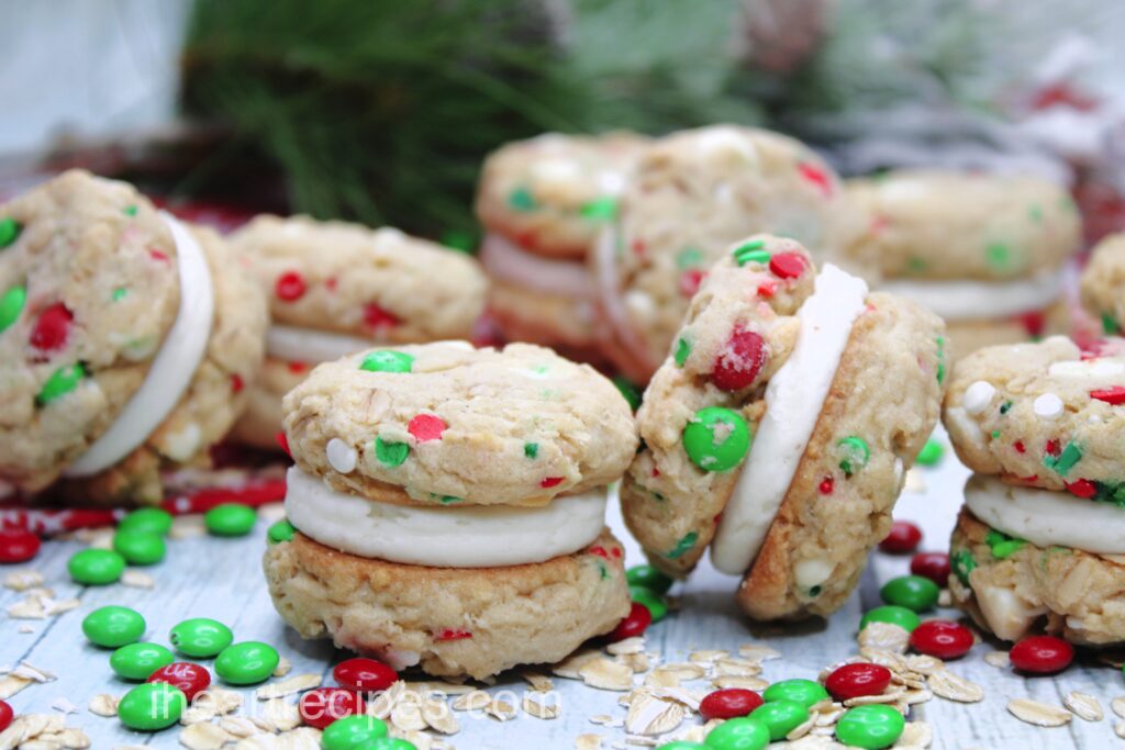 Christmas Oatmeal Cookie Sandwiches scattered on a wooden table alongside red and green M&M's and oats. 