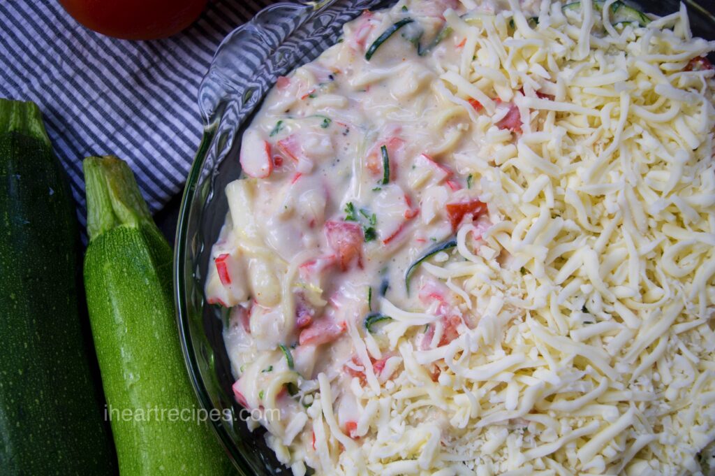 A glass casserole dish filled with creamy zucchini and crab alfredo casserole, topped with shredded cheese. 