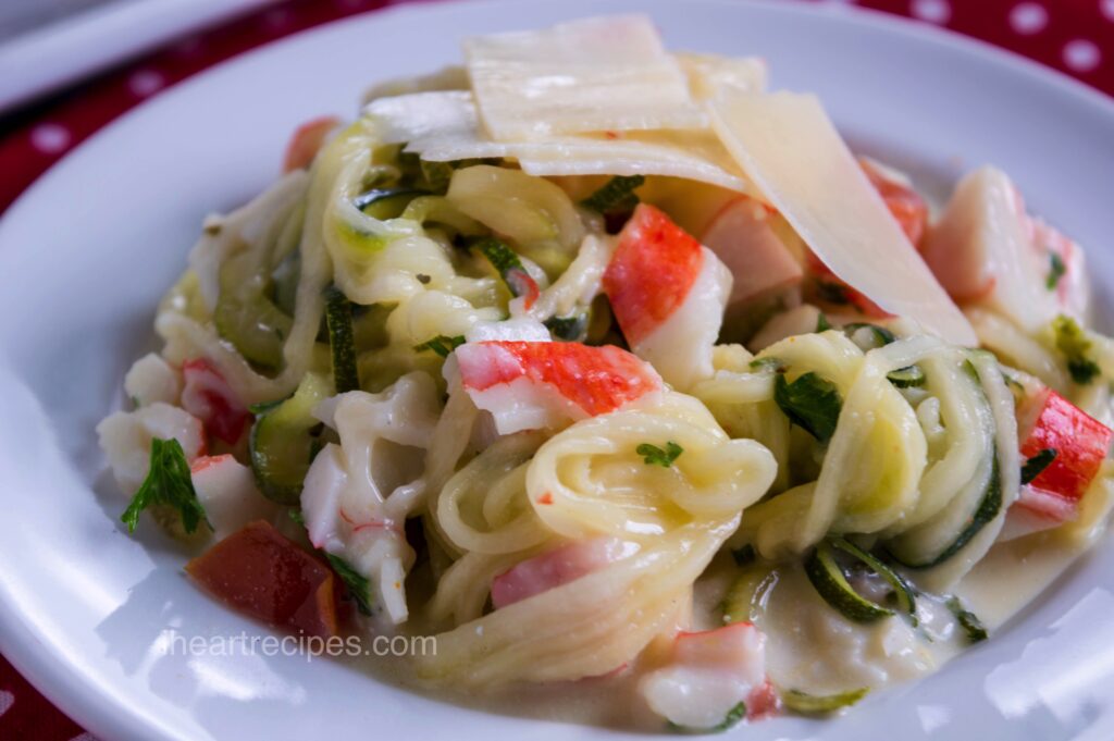 A close-up image creamy zucchini and crab Alfredo casserole topped with parmesan shavings served in a white pasta bowl.