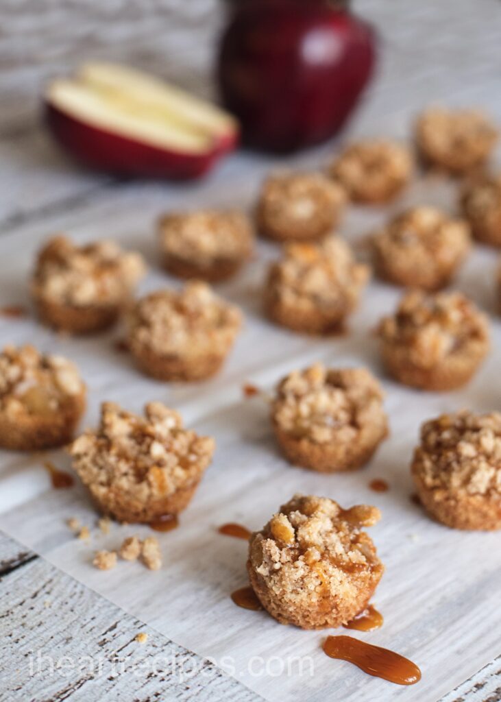 Rows of mini caramel apple crisps are arranged on a long piece of parchment paper set on a wooden counter.  