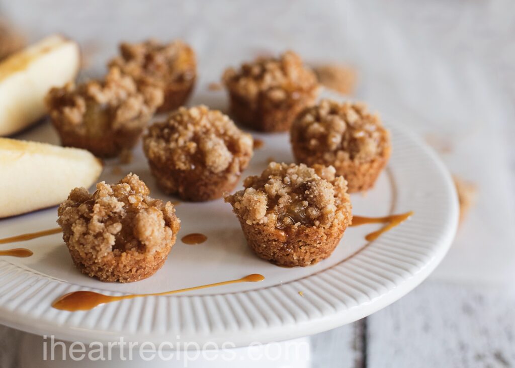 Mini Caramel Apple Crisps and apple wedges served on an elegant white platter. Caramel is drizzled over the crisps. 