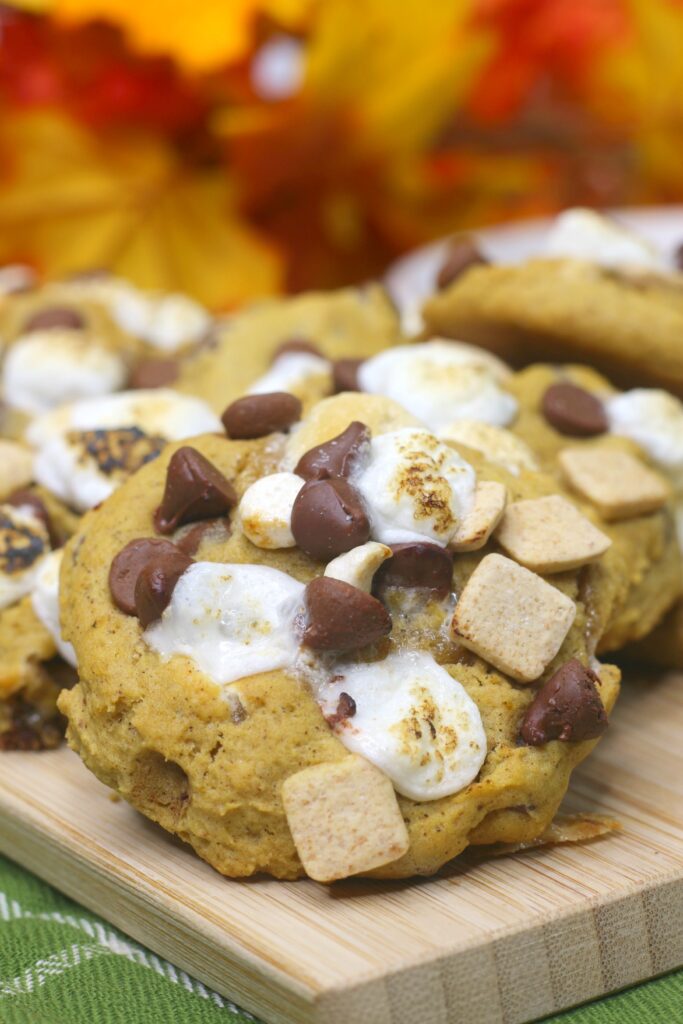 A close up of Pumpkin S'mores Cookies. The golden cookie is covered in melted marshmallows, soft chocolate chips and s'mores baking chips. 