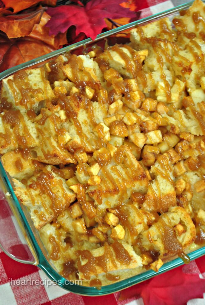An overhead image of Overnight Caramel Apple French Toast Casserole in a glass dish and drizzled with caramel. Festive fall leaves are nearby. 