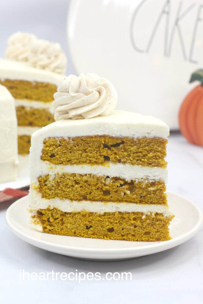 A close up of a piece of three-layered pumpkin cake on a white plate. The layers are frosted with cream cheese frosting. 