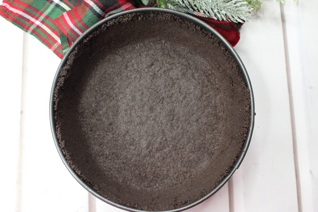 An Oreo cookie crust pressed into a round metal bake dish. 