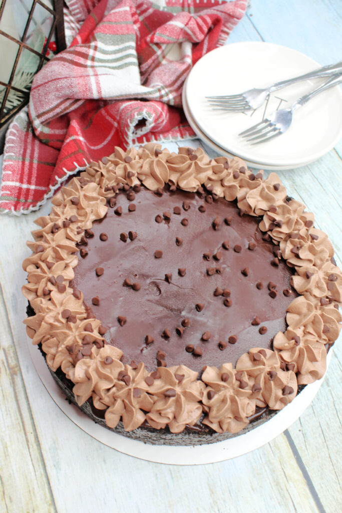 A round chocolate cheesecake decorated with chocolate chips and creamy light brown whipped cream piped along the outside edge.