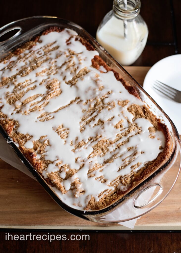 Old Fashioned Banana Crumb Cake in a rectangular glass bake dish. The golden dessert is drizzled with bright white icing. 