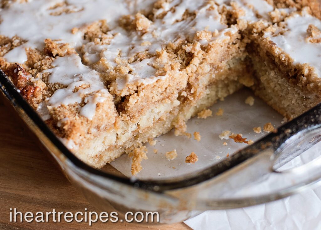 A glass bake dish filled with golden banana crumb cake drizzled with glaze. 