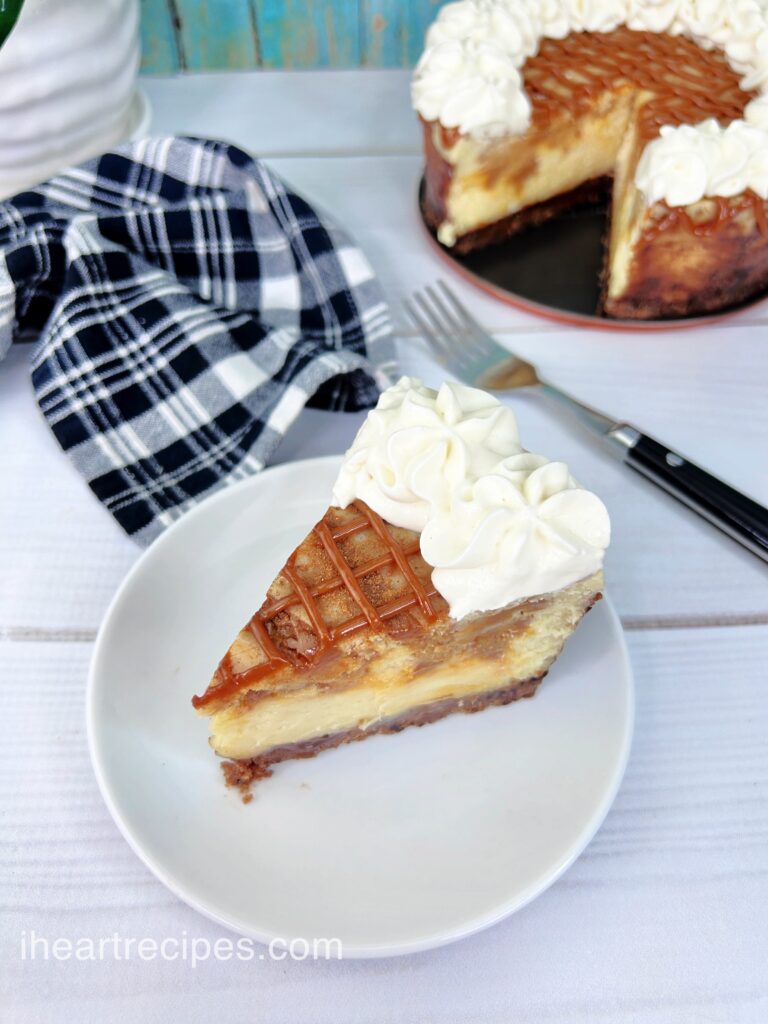 A slice of creamy cheesecake with a criss-cross pattern of dulce de leche across the top and dollop of whipped cream. 