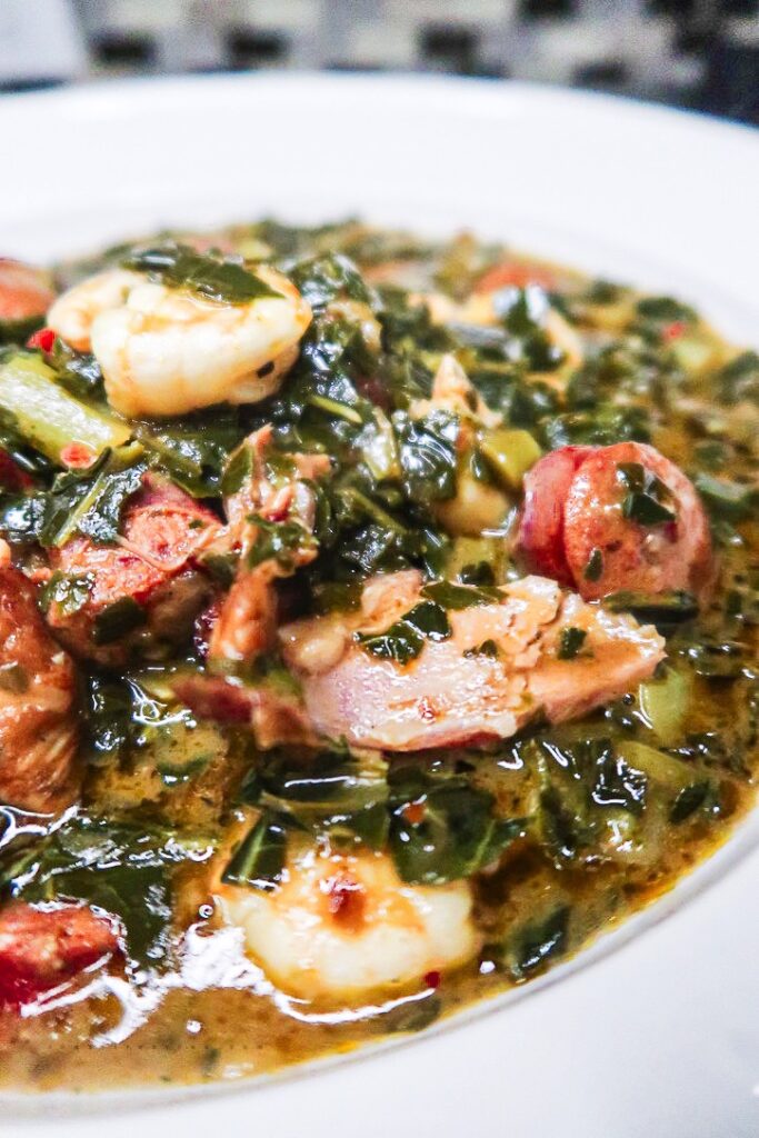 A closeup of a colorful bowl of Gumbo Greens. Golden broth, bright greens and tender meat fill a white bowl. 