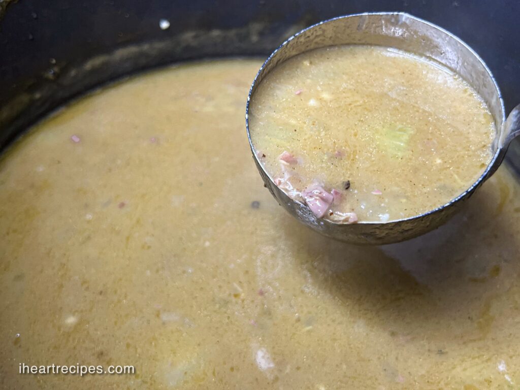 A ladle full of golden Southern Giblet Gravy over a large pot. 