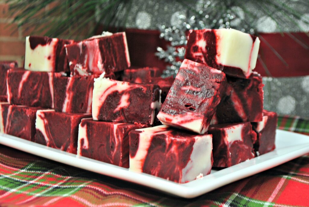 Cubes of red velvet swirl fudge stacked on a rectangular white platter.