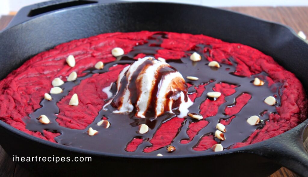 A red velvet cookie drizzled with chocolate sauce and served in a cast iron skillet. 