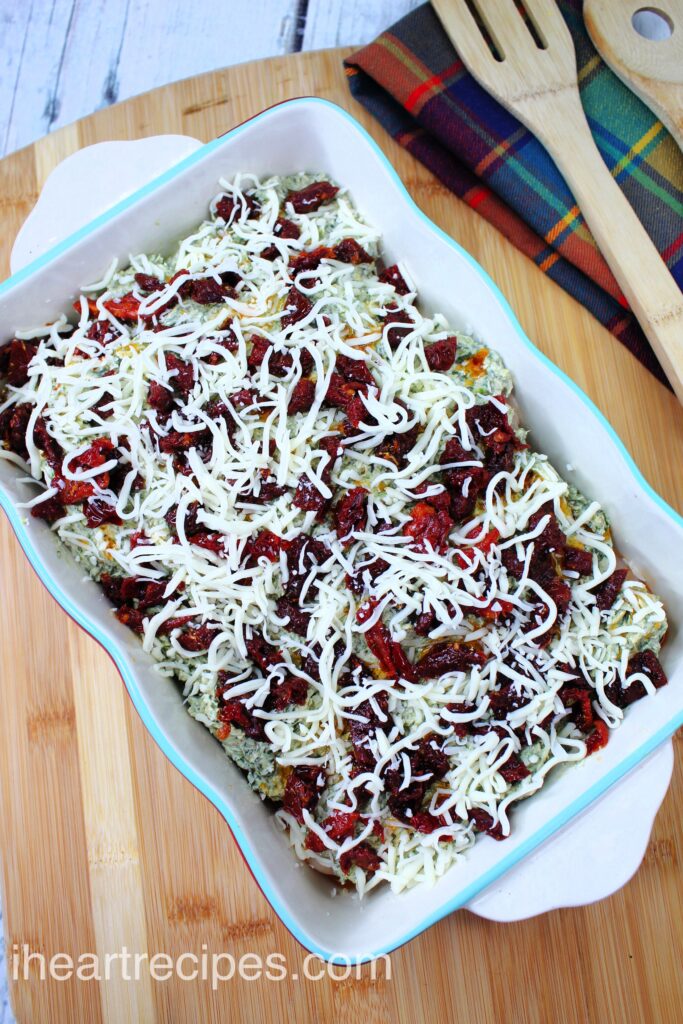 A layer of shredded white cheese and bright red sun-dried tomatoes arranged in a casserole dish. 