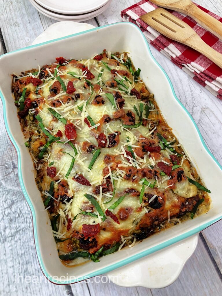 Baked Tuscan Chicken Casserole served in a turquoise and white casserole dish. The casserole is topped with gooey cheese and fresh basil shreds. 